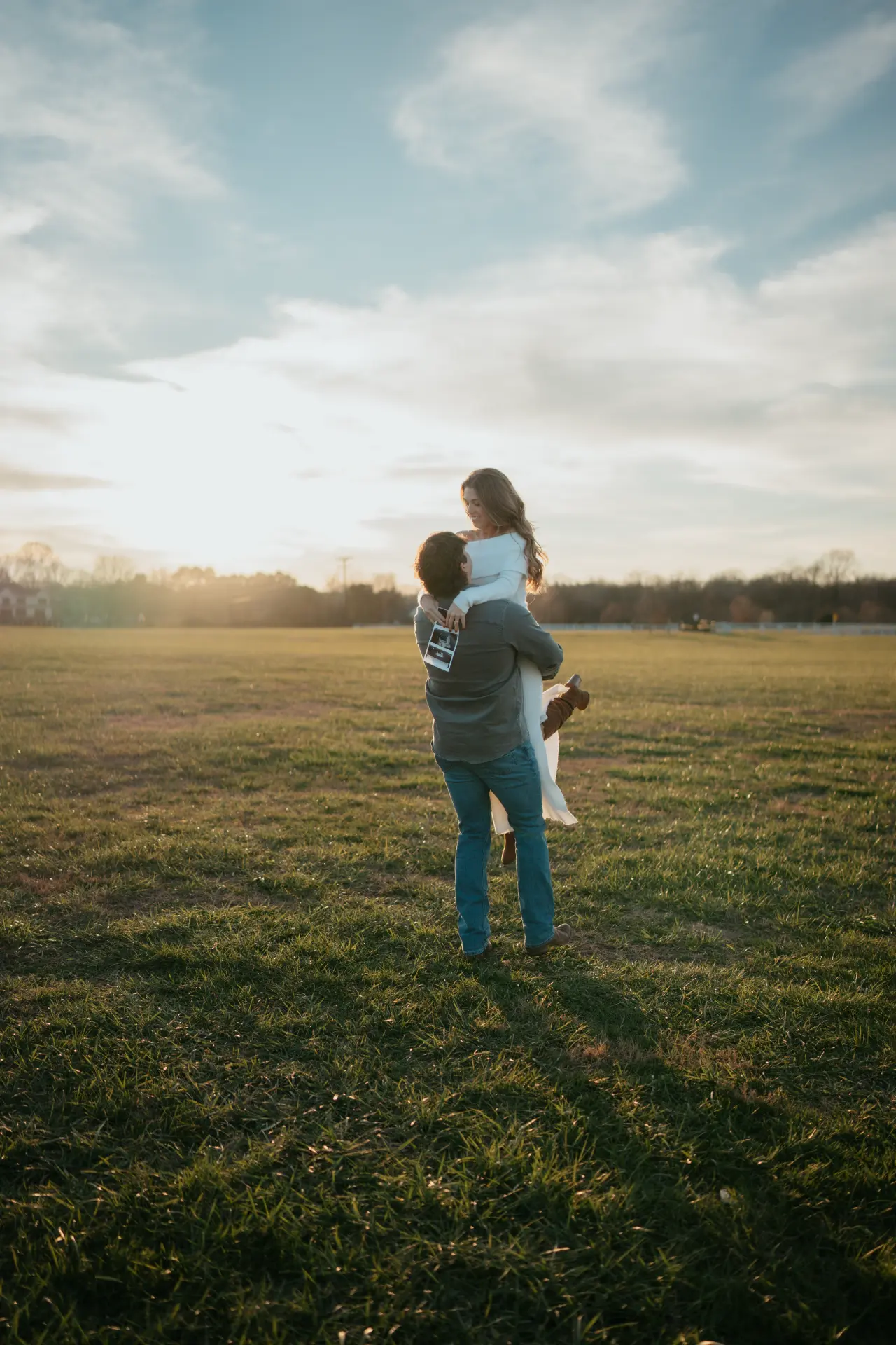 Tyler lifting Morgan in an open field at sunset