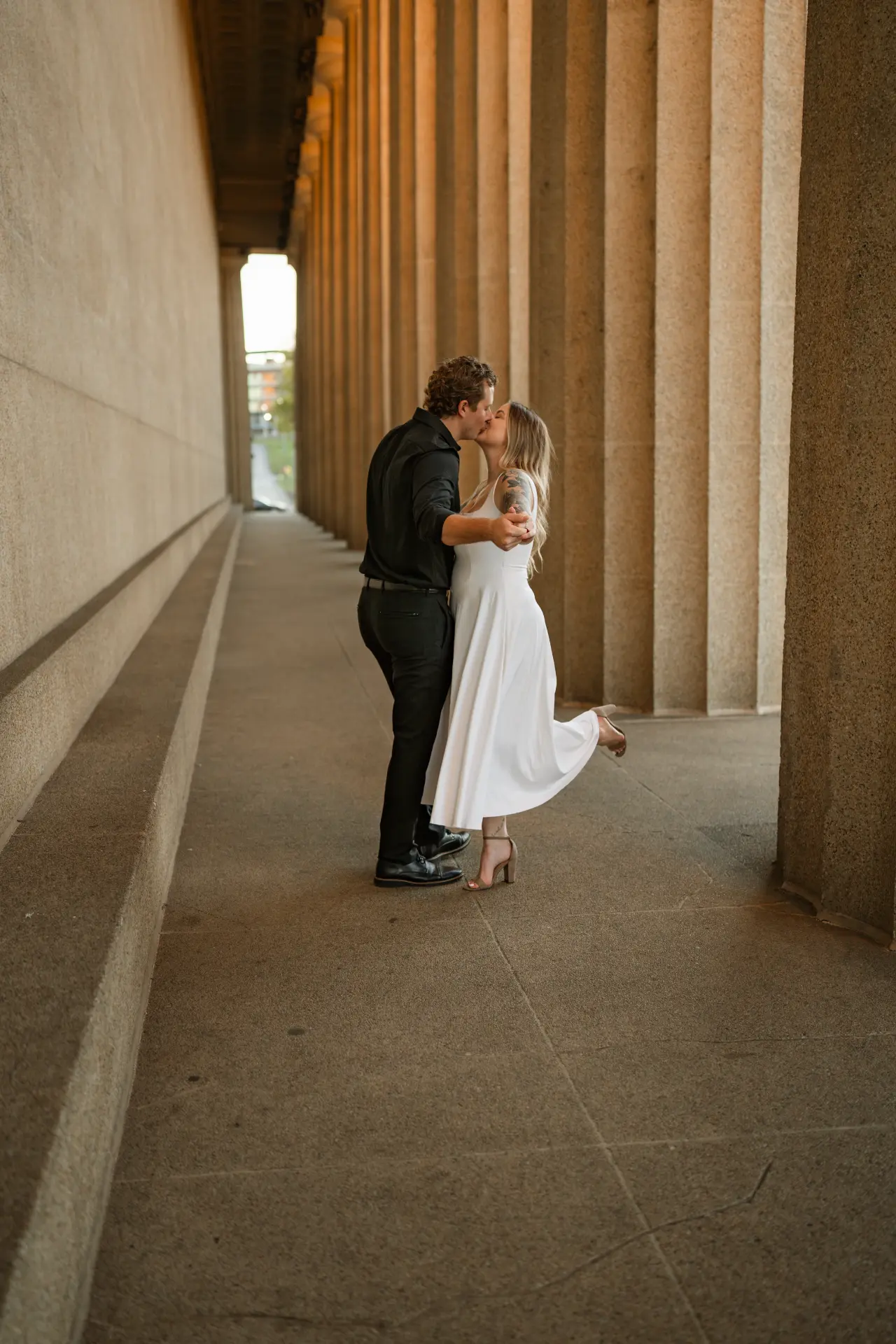 Emily and Alex kissing between the columns of the Parthenon at sunset during their engagement session