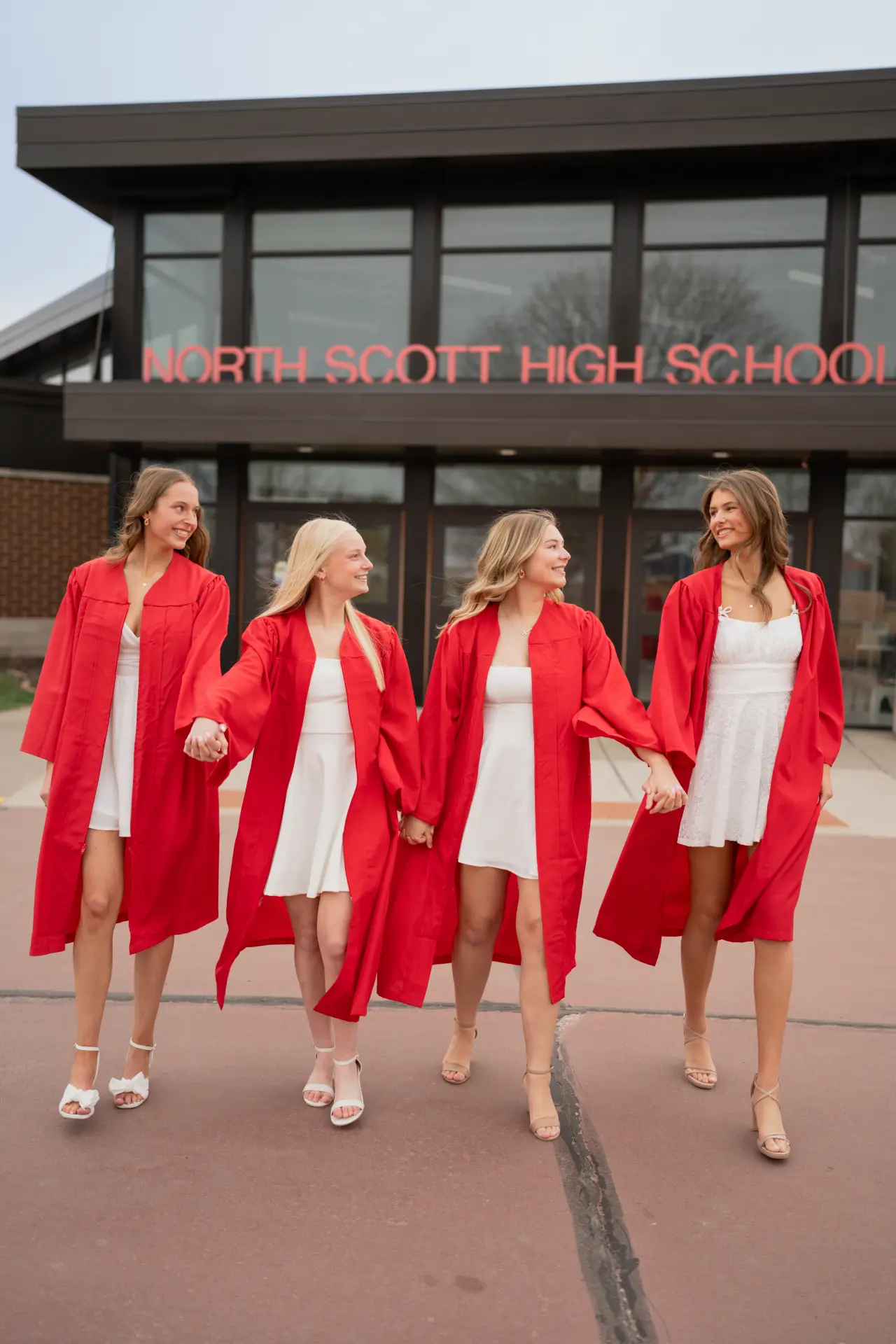 Abbey Hayes and friends in red graduation gowns walking in front of North Scott High School