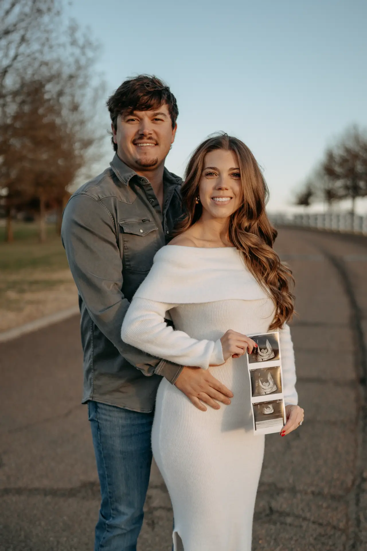 Tyler and Morgan smiling together holding ultrasound photos
