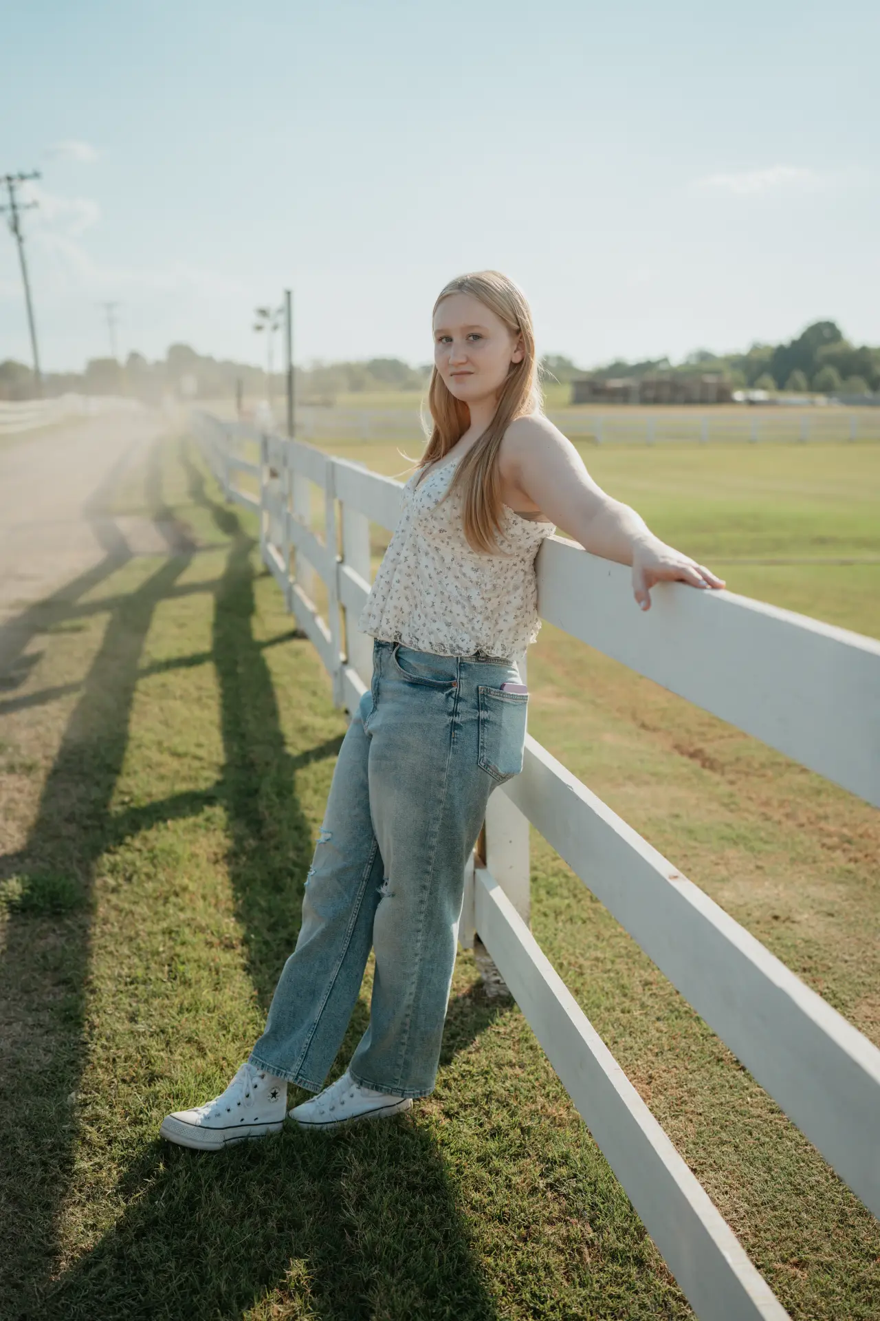 Senior leaning back against a white fence line at golden hour