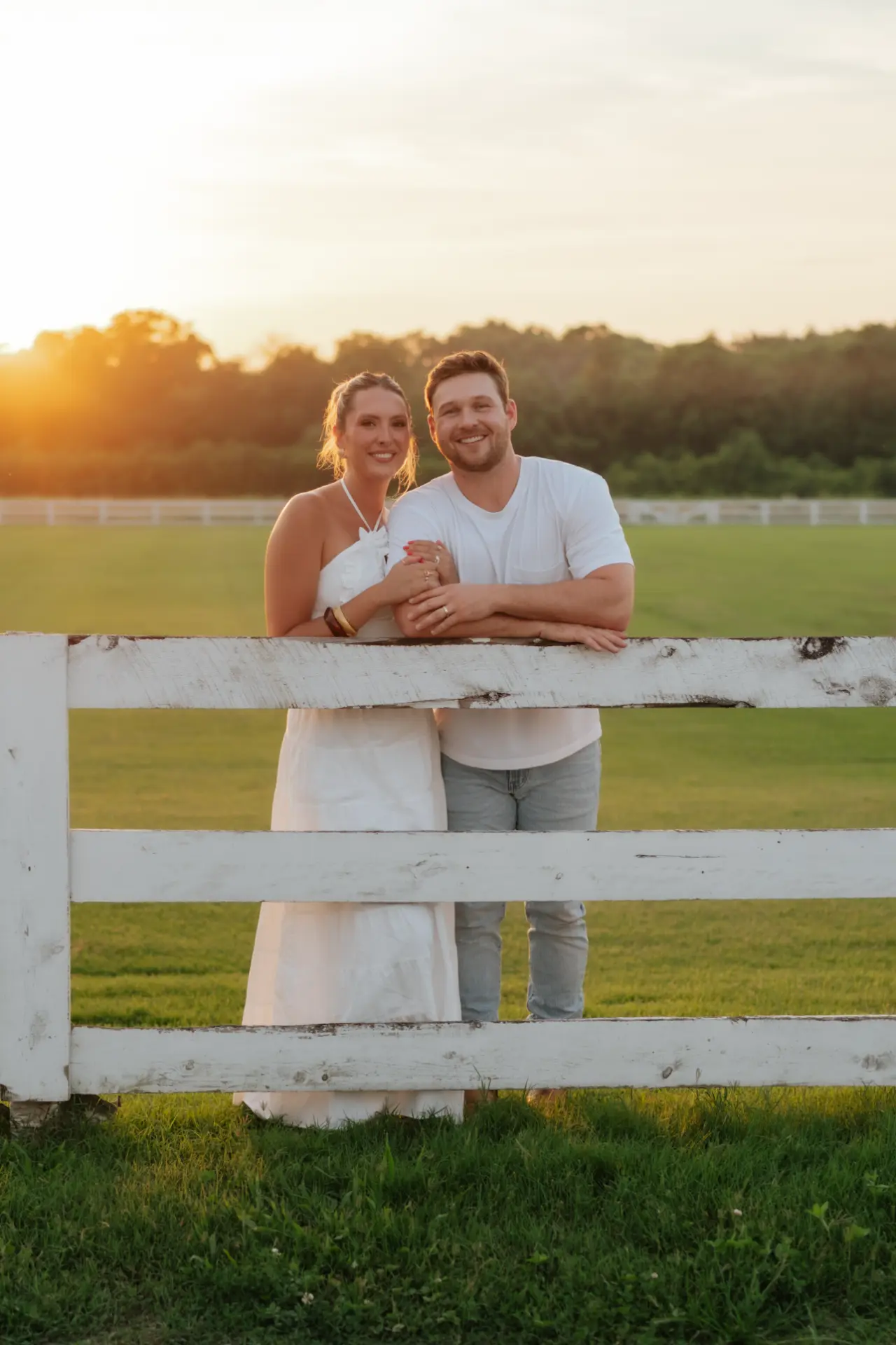Mandy and Taylor leaning on a white pasture fence at sunset