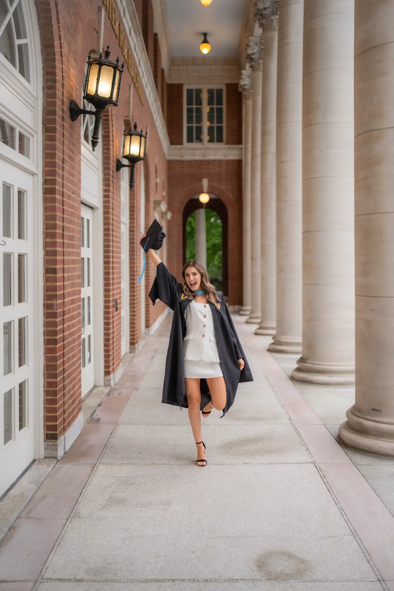 Graduate celebrating with her cap raised in a campus colonnade