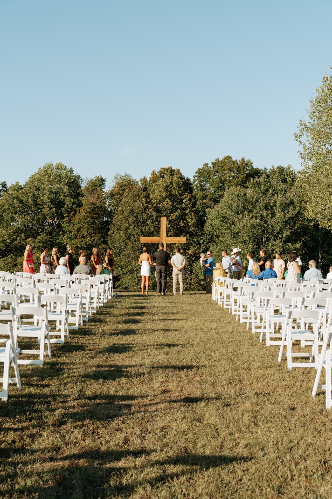 Ryan and Lizzie walking the grass aisle toward the timber cross with guests standing