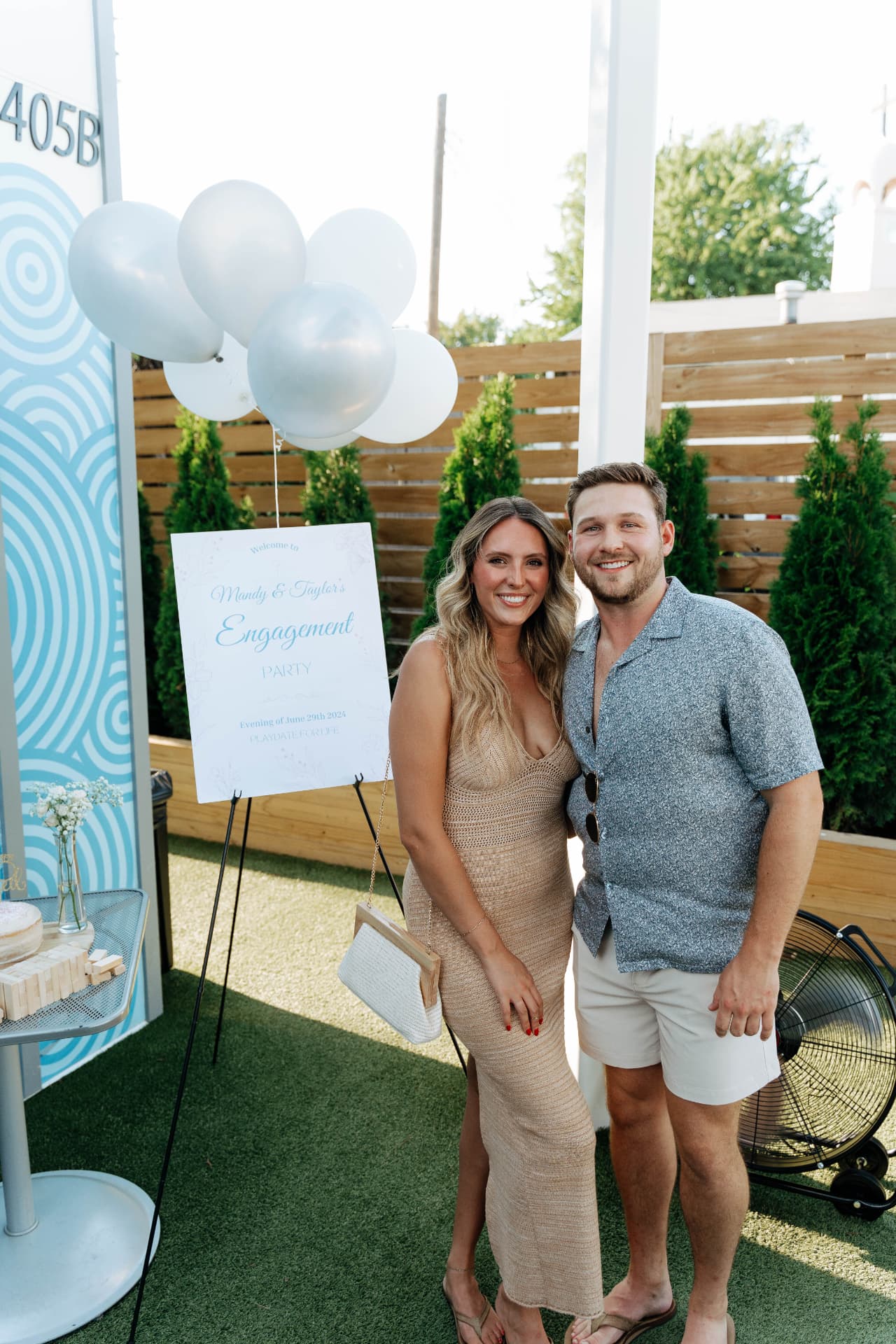 Mandy and Taylor smiling together beside their engagement party welcome sign